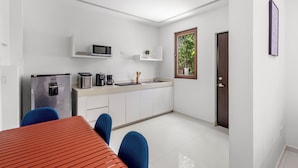 A modern kitchen with white cabinets, a microwave, a toaster, and a coffee maker. There is a dining table with blue chairs and a red-striped tablecloth. - Senderos De Ciudad Mayakoba (Playa del Carmen)