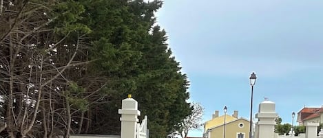 A gated driveway leading to a building with a white fence and a street lamp.