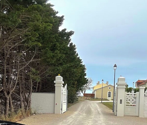 A gated driveway leading to a building with a white fence and a street lamp.