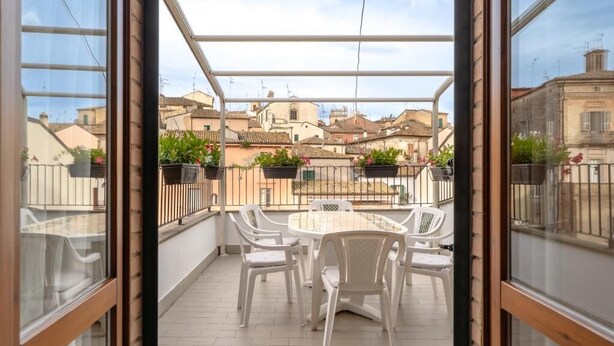 Un balcon extérieur abrité, doté d’une table et de chaises, qui offre une vue sur un quartier résidentiel.