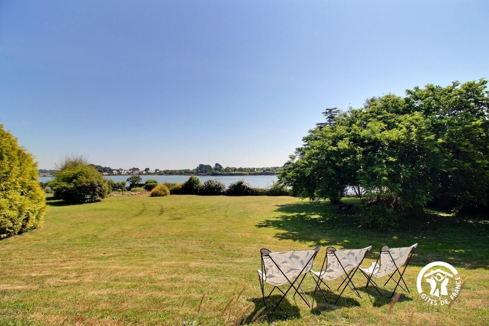 A grassy area with a lake and trees in the background. There are two camping chairs in the foreground.