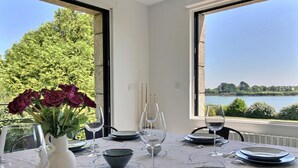 A dining table set with plates, bowls, and wine glasses, overlooking a lake with trees and a clear sky. - Ty Bayon - BELZ - Gîte (BELZ)