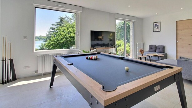 A modern living room with a pool table, large windows, a television, and a cozy seating area. - Ty Bayon - BELZ - Gîte (BELZ)