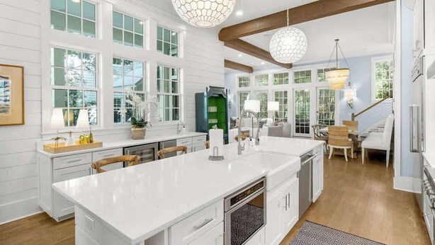 A modern kitchen with a large island, white cabinetry, and a dining area with a staircase.