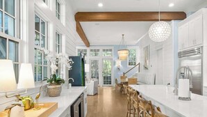A modern kitchen with white cabinetry, a wooden countertop, and a dining area with wooden chairs.