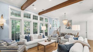 A spacious living room with a high ceiling, large windows, and a staircase leading to an upper level.