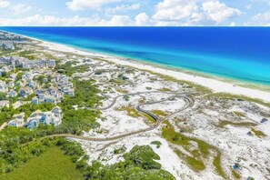 Vue aérienne d’une zone résidentielle côtière, avec des maisons, une route sinueuse et une plage.