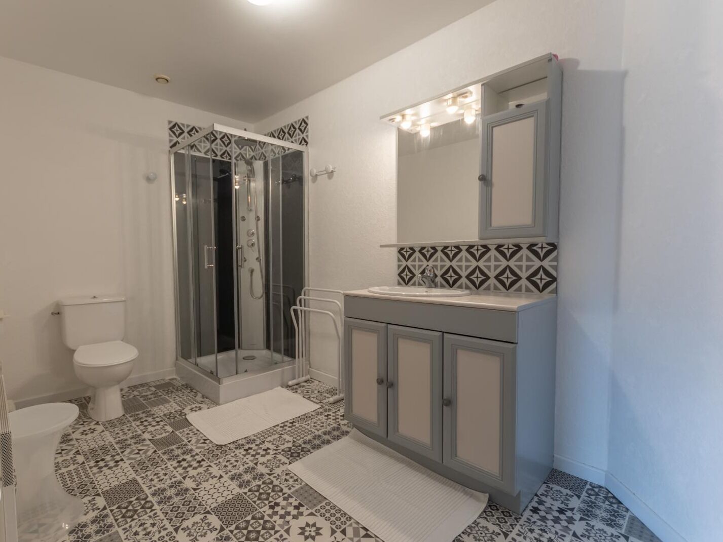 Een badkamer met toilet, douchecabine, wastafel met spiegel en vloertegels met patroon.