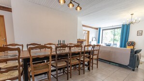 Un comedor con una mesa redonda y sillas de madera, una araña y un sofá con una manta.