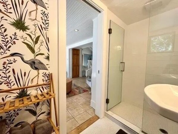 A bathroom with a glass shower enclosure, a white sink, and a wooden rack with towels.