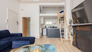 Una sala moderna con un sofá azul, una mesa de centro de vidrio y una escalera de madera que conduce a un nivel superior.