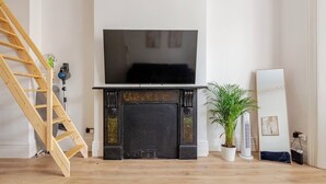 Una sala de estar con chimenea, un televisor montado encima, una escalera, una planta en maceta y un espejo grande.
