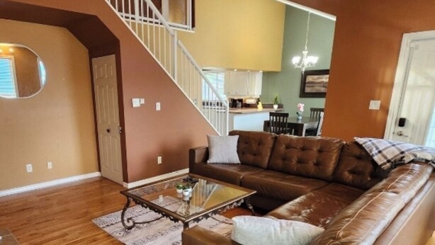 A spacious living room with a brown leather sofa, a glass coffee table, and a wooden floor. A staircase leads to an upper level, and a kitchen is visible in the background. - Lake Escape 1-minute walk to beach/Main st (Winnipeg Beach)