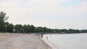 A beach with people walking along the shore and a body of water in the background. - Lake Escape 1-minute walk to beach/Main st (Winnipeg Beach)