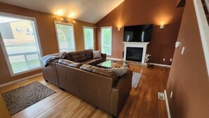 A living room with a sectional sofa, a fireplace, and a TV mounted above it. - Lake Escape 1-minute walk to beach/Main st (Winnipeg Beach)