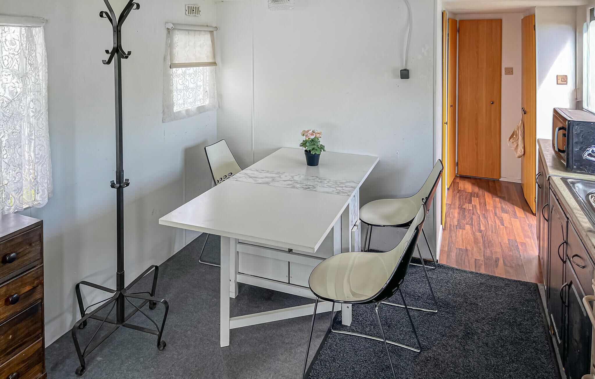 A compact room with a white table, two chairs, a floor lamp, a potted plant, and a wooden cabinet.