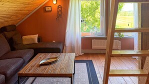 A cozy room with a sloped ceiling, a wooden table with a decorative tray, a cushioned sofa, and a window with a view of greenery. - 1 bedroom nice apartment in Aneby (Aneby)