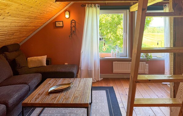 Una habitación acogedora con techo inclinado, una mesa de madera con una bandeja decorativa, un sofá con cojines y una ventana con vistas a zonas verdes.