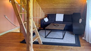 A loft-style room with a wooden ceiling, a dark gray sofa, a small wooden table, and a ladder. - 1 bedroom nice apartment in Aneby (Aneby)
