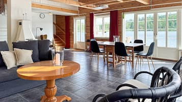 A spacious living area with a wooden ceiling, a round wooden table, a sofa, and a dining table with chairs.