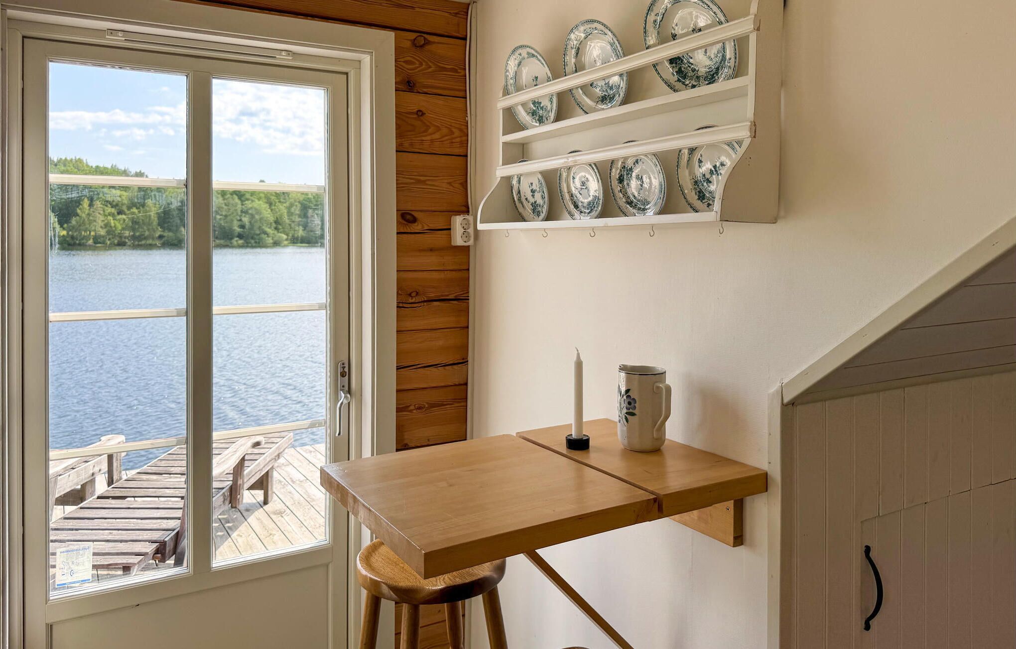 A kitchen with a wooden table, a hanging shelf with plates, and a view of a lake through a window.
