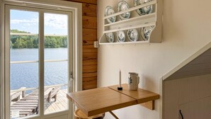 A kitchen with a wooden table, a hanging shelf with plates, and a view of a lake through a window. - Lovely home in Gränna with house sea view (Gränna)
