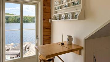 A kitchen with a wooden table, a hanging shelf with plates, and a view of a lake through a window.