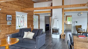 A cozy living room with a grey sofa, a round wooden table, and a white fireplace. - Lovely home in Gränna with house sea view (Gränna)
