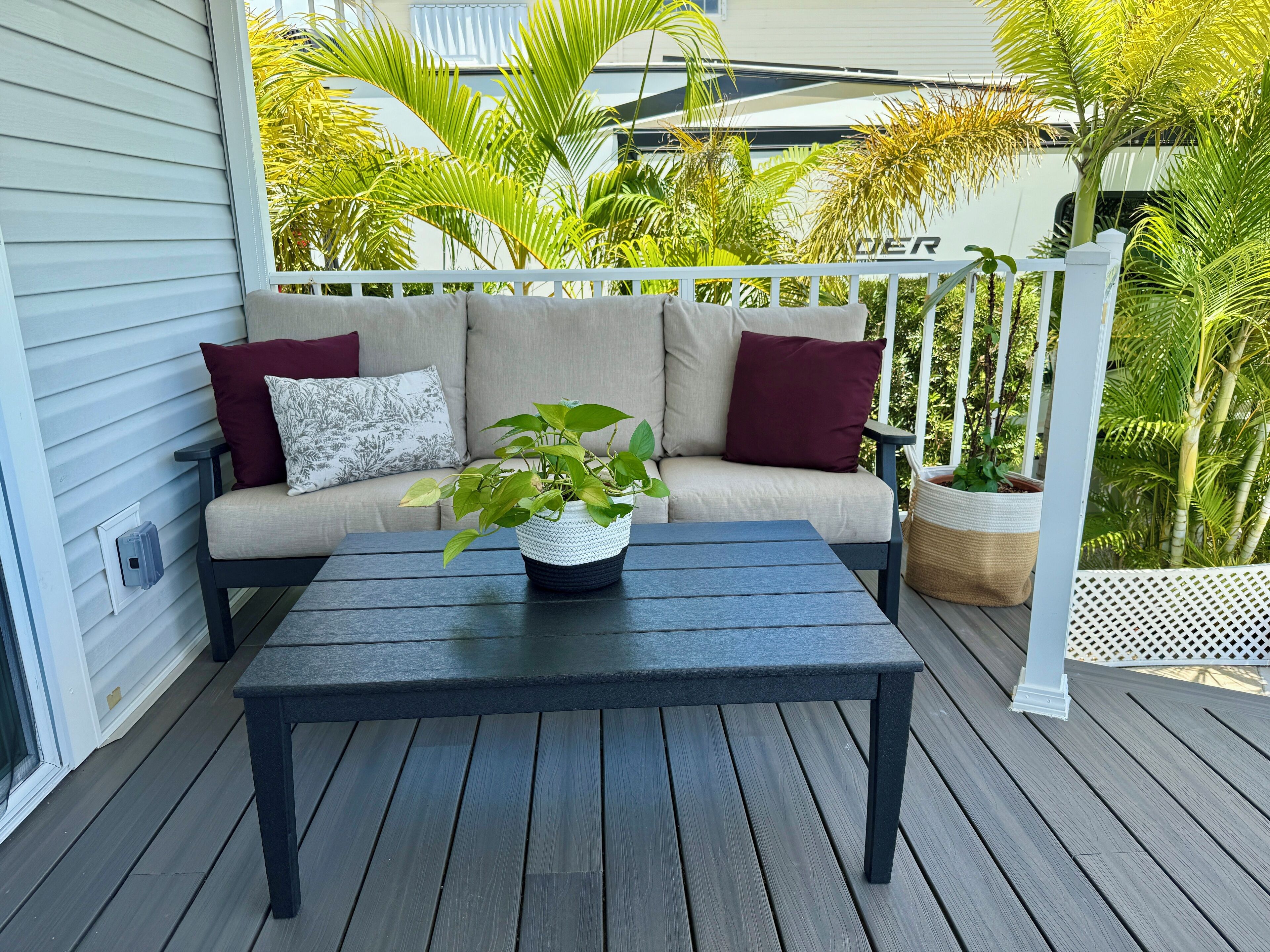 Een overdekt terras met een donker houten tafel en een beige bank met rode kussens.