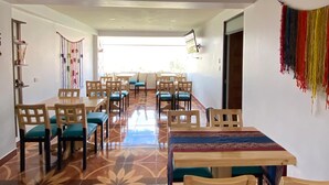 Un espace repas avec des tables et des chaises en bois, un sol à motifs et une décoration murale colorée.