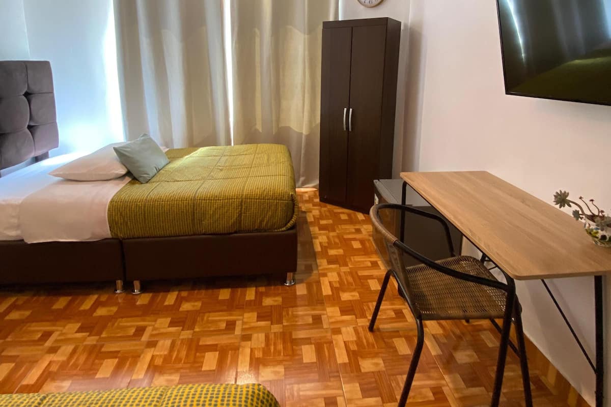 Un dormitori modern amb llit, escriptori, cadira, armari i televisió penjada a la paret.