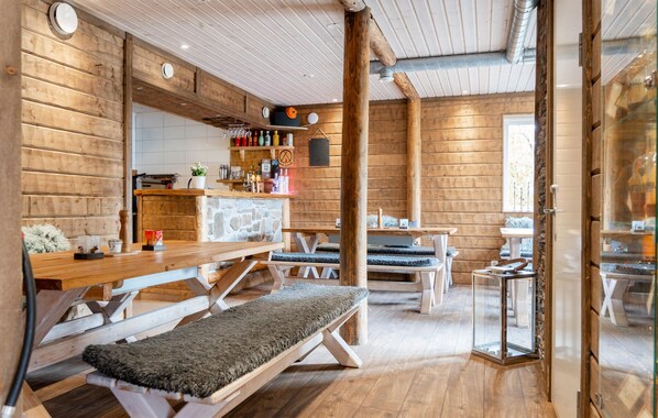 Interior acogedor estilo cabaña con paredes de madera y un muro de acento de piedra, que presenta un banco, mesas y una zona con cerramiento de vidrio.