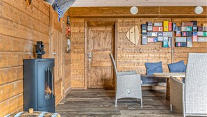 Ein gemütliches Blockhaus-Interieur mit Holzwand, einem schwarzen Holzofen, Korbmöbeln und einer Wandvitrine mit verschiedenen Gegenständen.