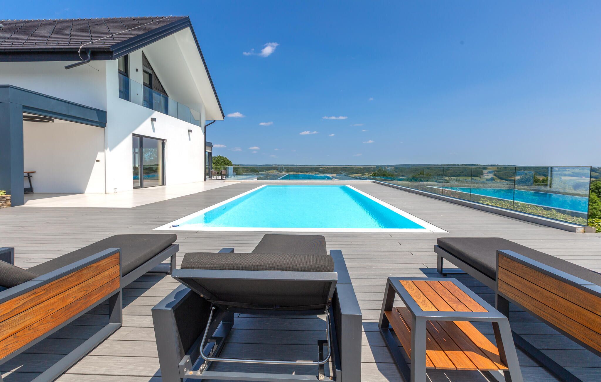 Un espace piscine extérieur moderne offrant une vue dégagée sur la mer, avec une terrasse en bois et des fauteuils confortables.