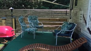 Une terrasse dotée d’un auvent, de deux chaises, d’un banc et d’un barbecue.