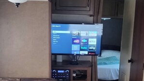 Un intérieur de camping-car compact comprenant un canapé, une petite table, un téléviseur permettant d’accéder aux services de diffusion en continu et un lit.