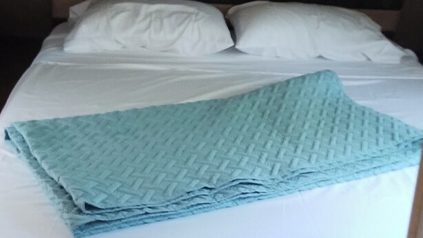 Un lit avec du linge de lit blanc et une couverture bleue, une tête de lit en bois et un plafond en bois.