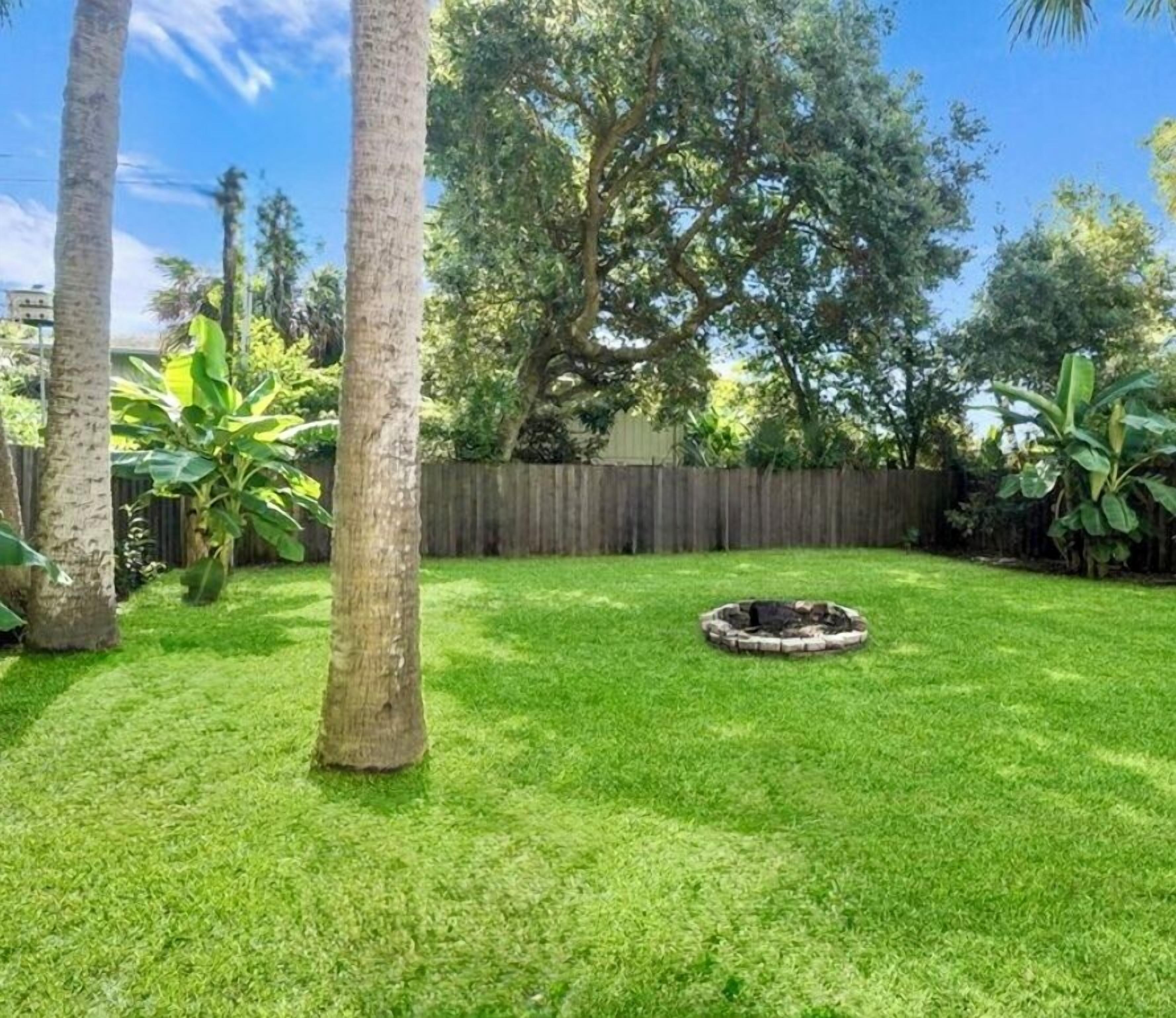 A backyard with a well-maintained lawn, a circular fire pit, and tall trees.