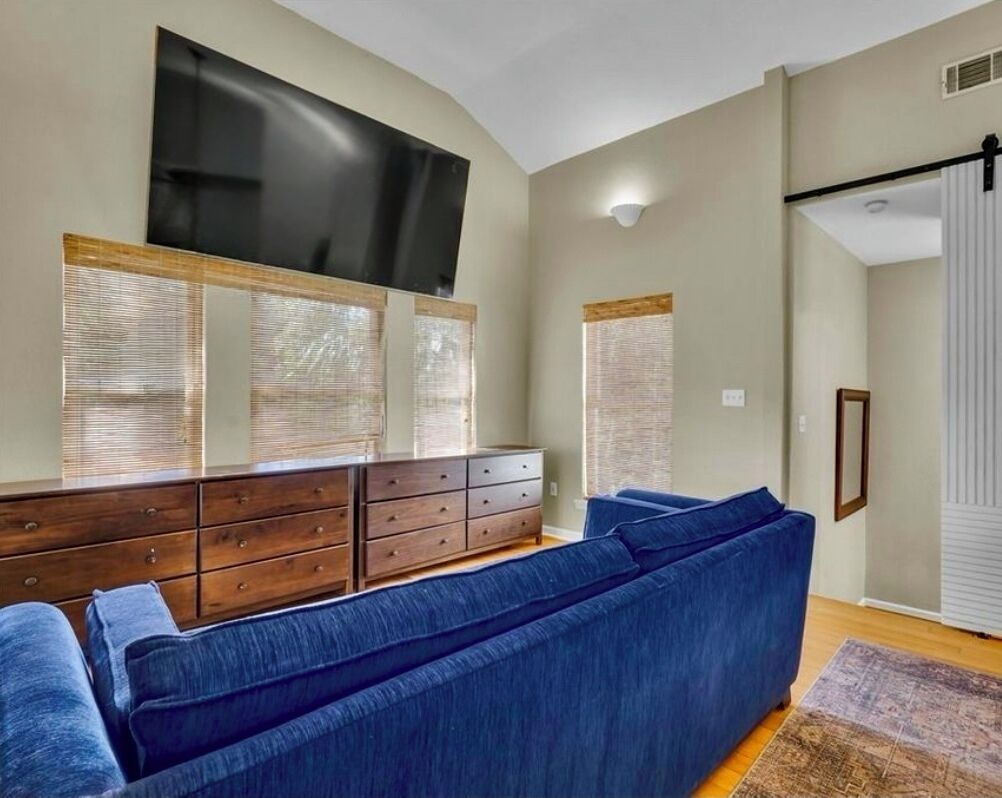 A living room with a blue sofa, wooden dresser, and a flat-screen TV mounted on the wall.