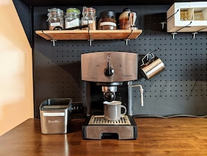 A coffee machine with a cup holder, a coffee grinder, and a shelf with jars of spices. - Mountain House of Wonder (Qualicum Beach)