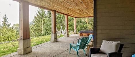 An outdoor patio with a wooden ceiling, concrete pillars, and a view of a garden. There are two chairs and a table.