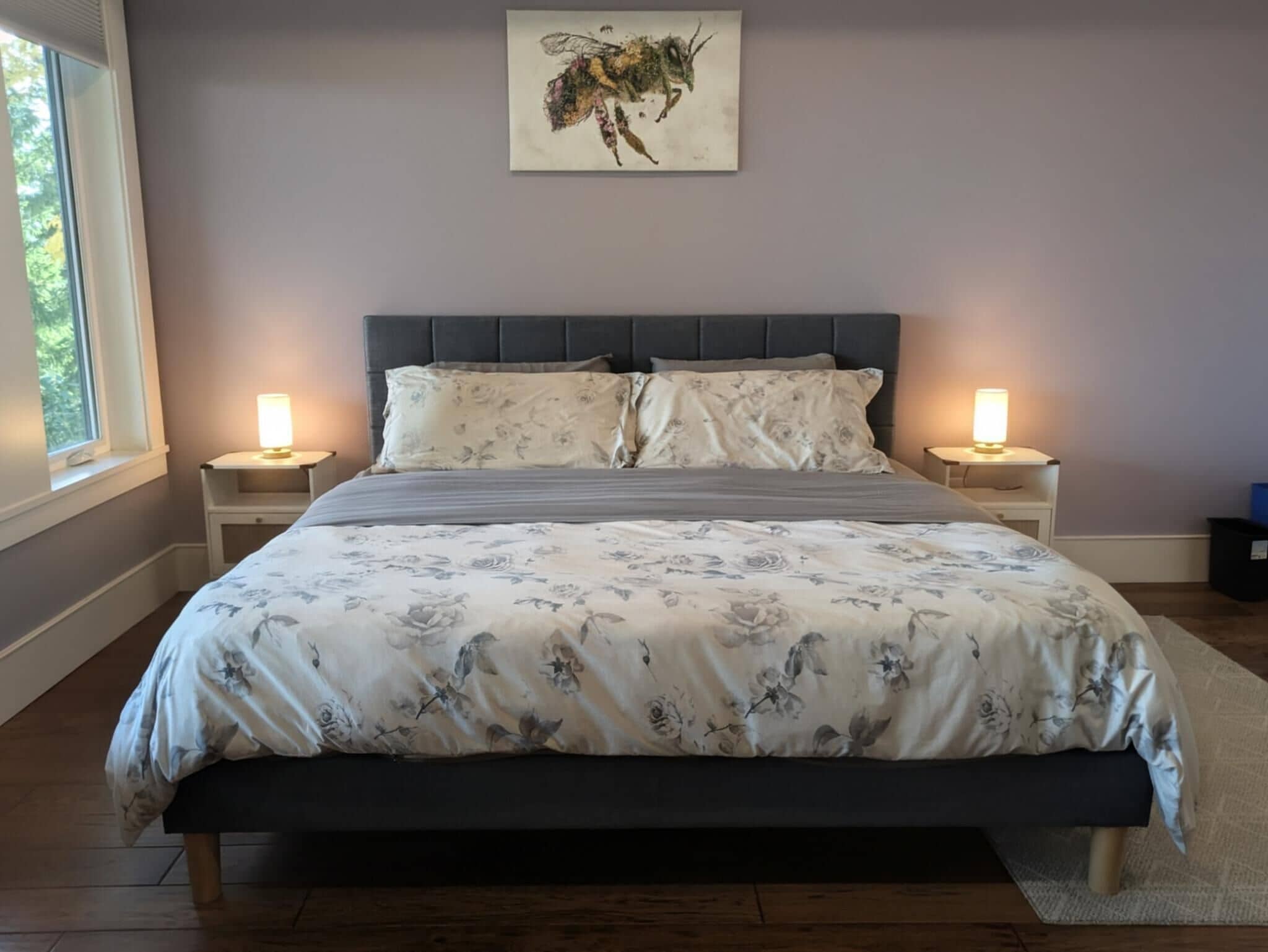 A bedroom with a large bed, two bedside tables with lamps, a headboard, and a window.