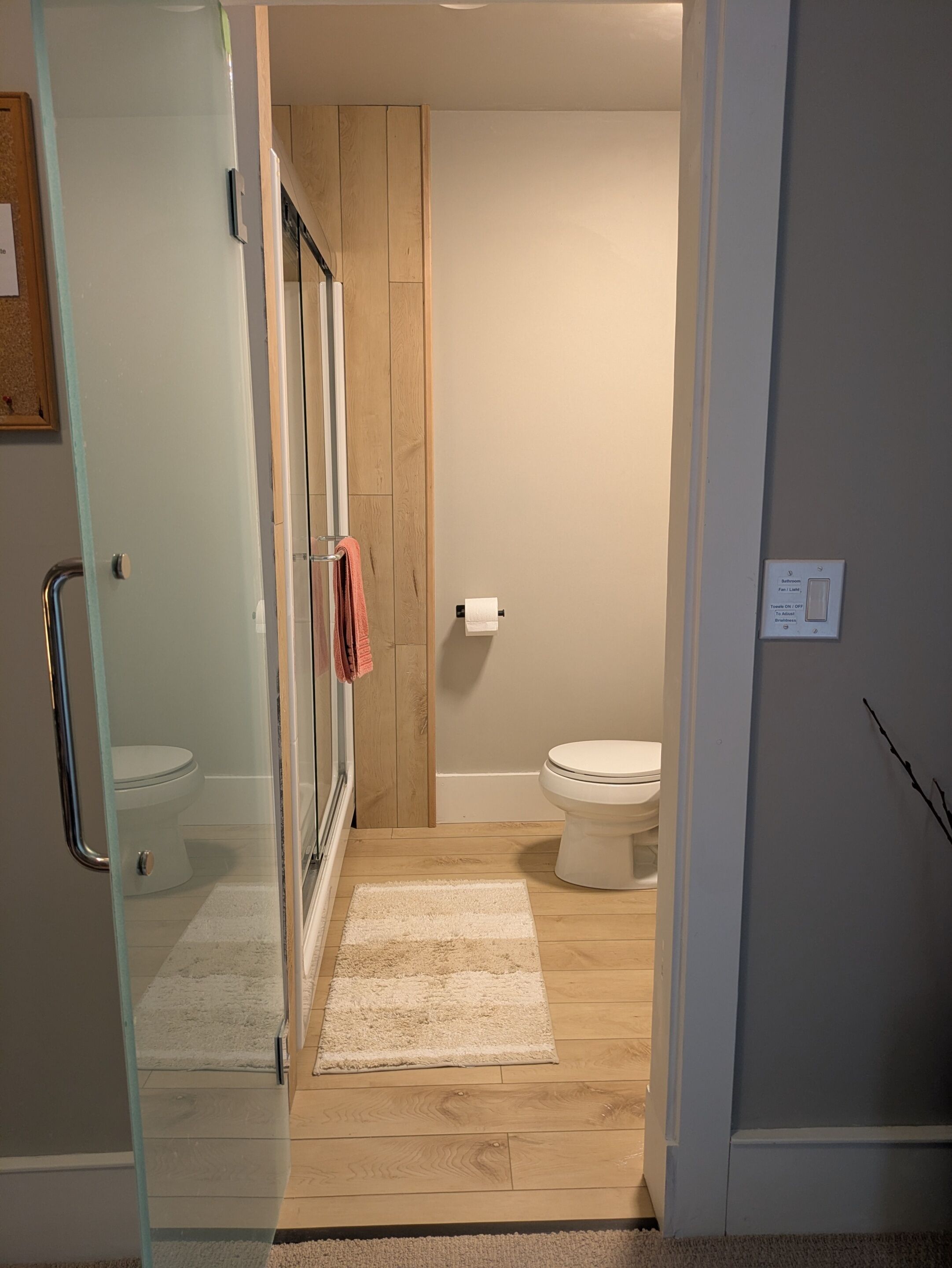 Un baño moderno con cabina de ducha de vidrio, suelo de madera y un inodoro blanco.
