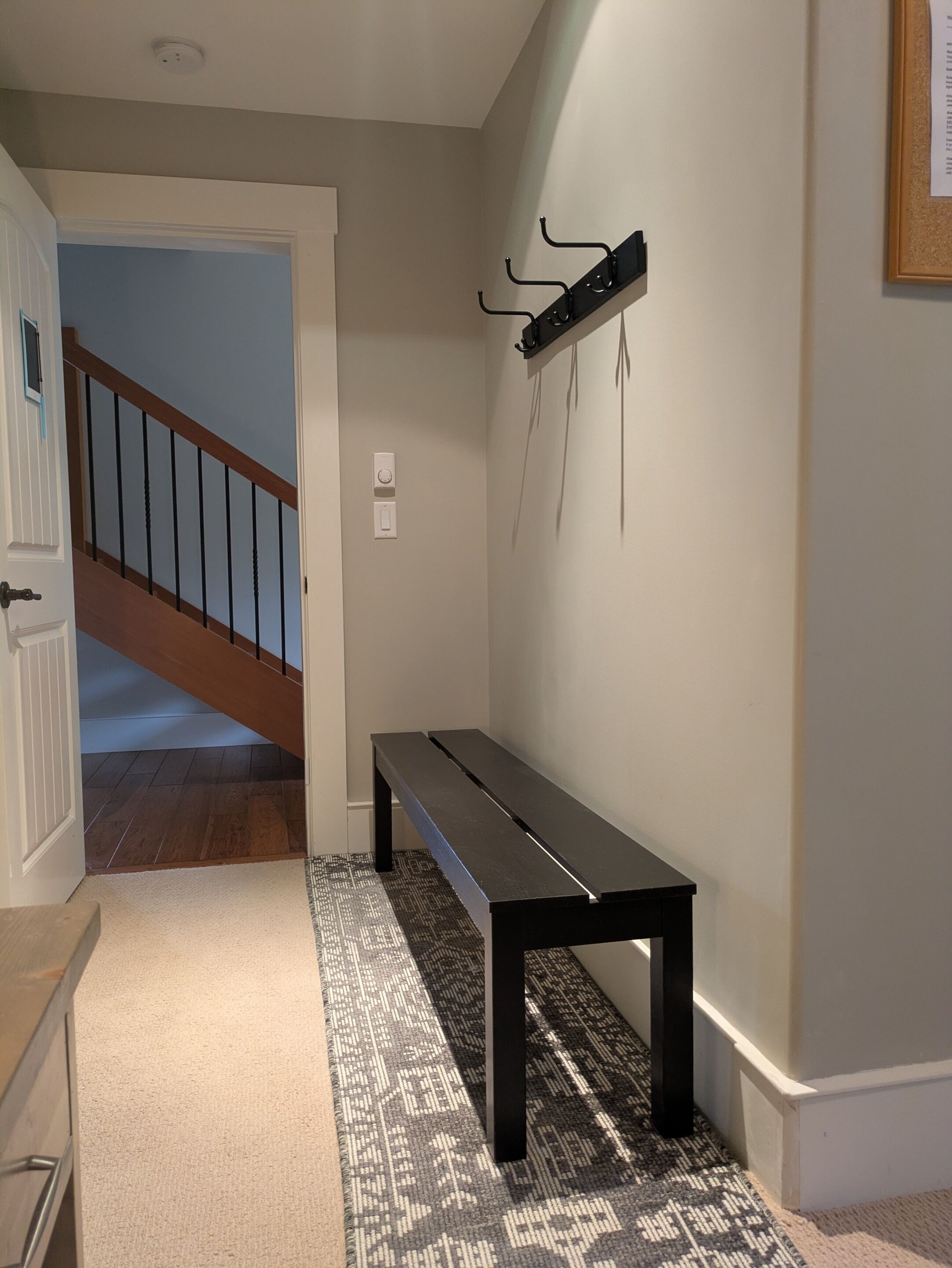 A hallway with a wooden staircase, a bench, a wall-mounted coat rack, and a patterned rug.