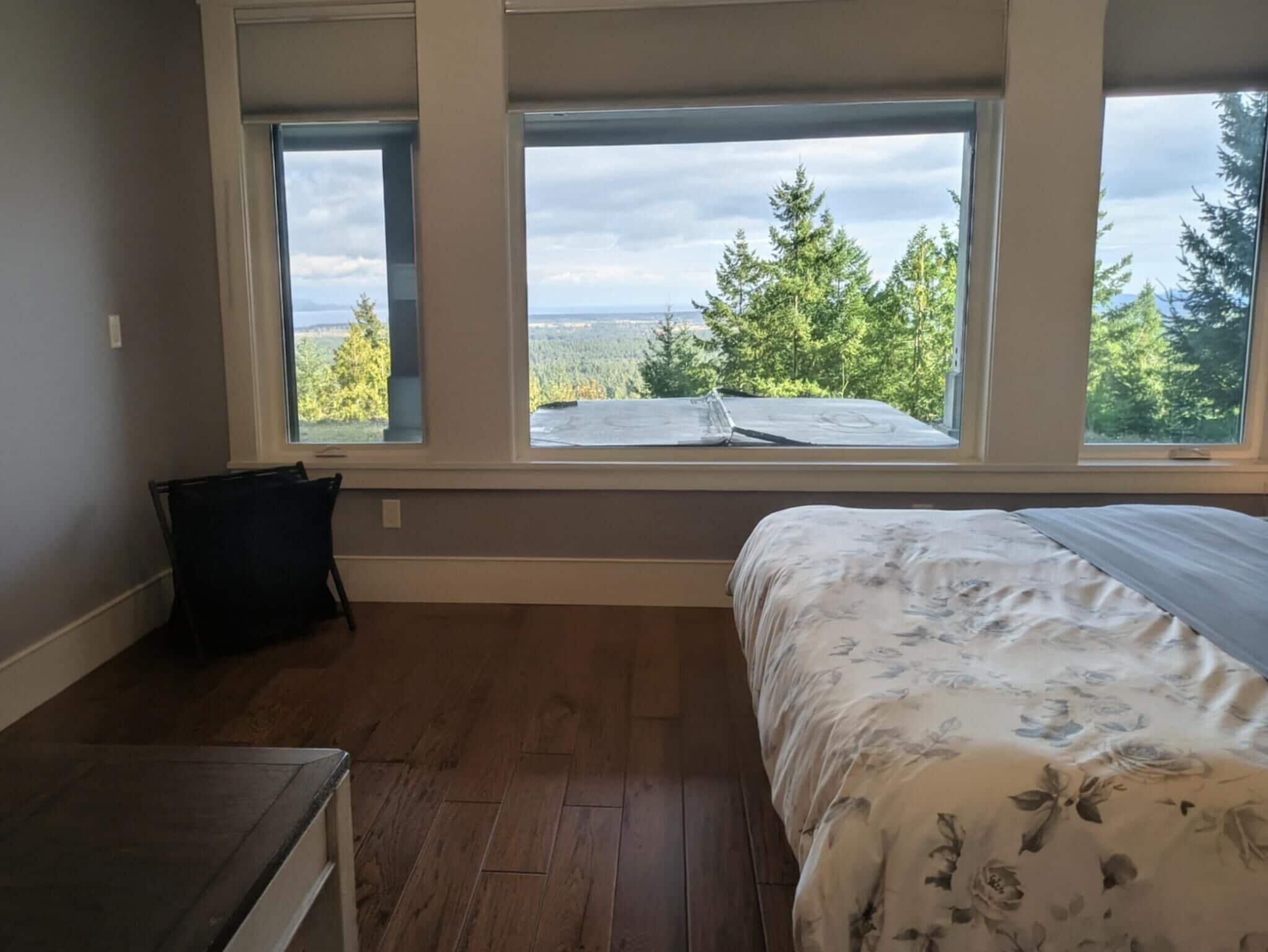 Un dormitorio con un ventanal grande, una cama con ropa de cama floral y suelo de madera.