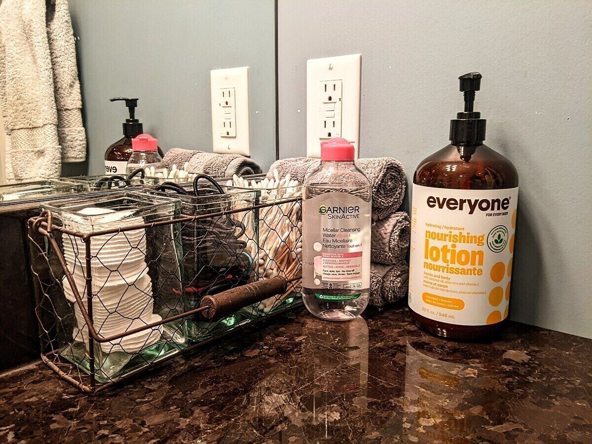 A bathroom counter with a glass dish rack, a bottle of Garnier Skinactive, and a bottle of nourishing lotion.
