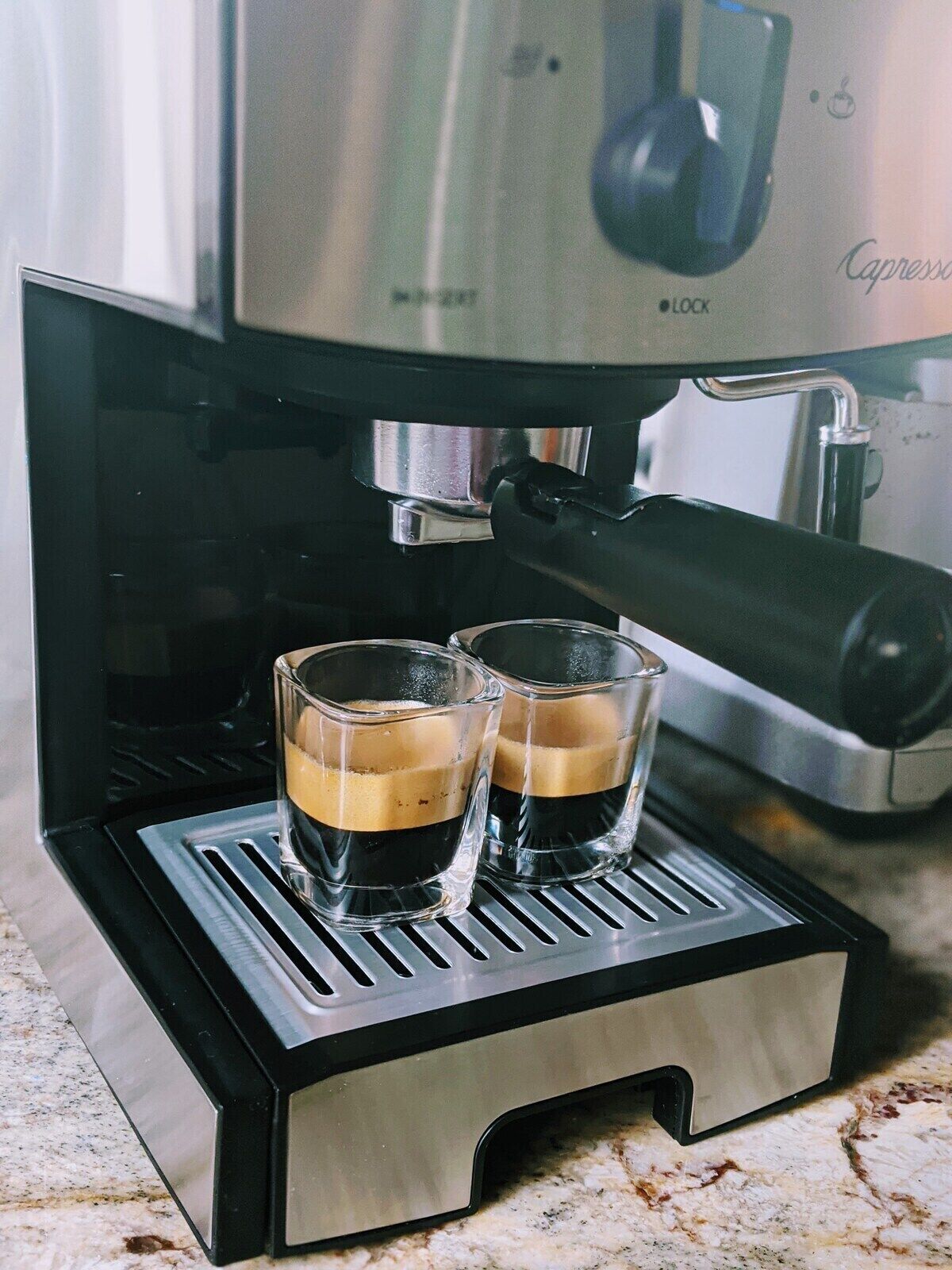 Una cafetera con dos tazas de café sobre la bandeja de goteo.