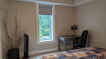 Un dormitorio con cama, escritorio, silla, radiador y ventana con vista a árboles.