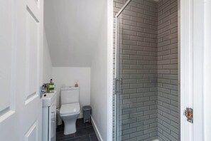 A bathroom with a toilet, a small trash bin, and a shower area with a glass door.