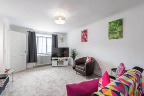 A living room with a television, a sofa, a chair, and a radiator.